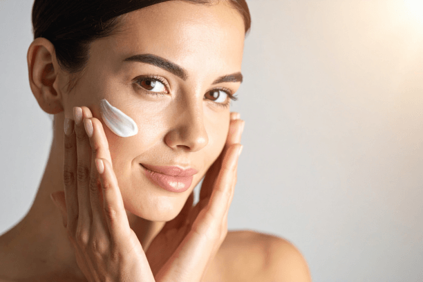 Kobieta nakłada krem na twarz, prezentując zdrową i promienną skórę. Idealne zdjęcie do artykułów o pielęgnacji skóry i kosmetykach.