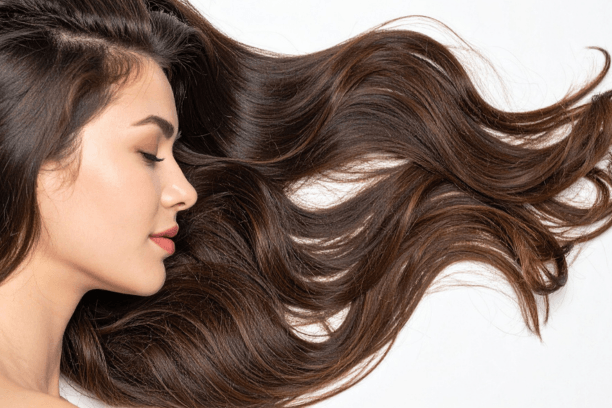 Kobieta z długimi, lśniącymi brązowymi włosami, patrząca w bok, na tle białej ściany. Włosy układają się w falujące pasma, podkreślające zdrowy wygląd i objętość.